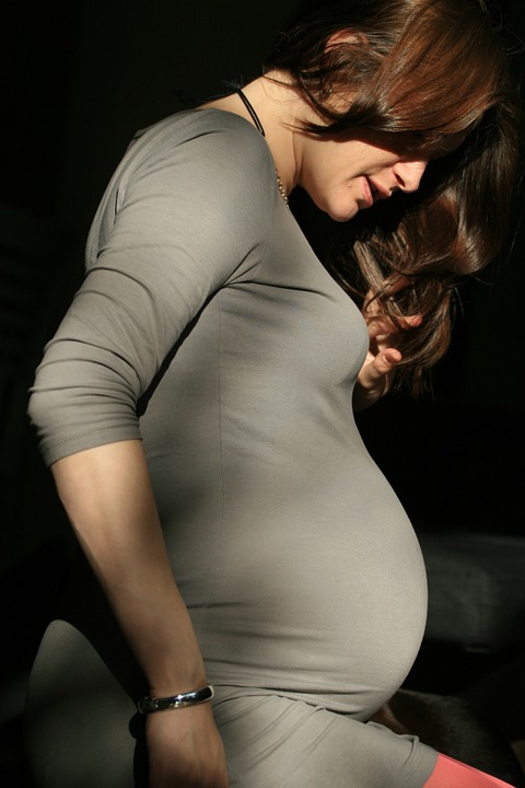 Těhotná žena v obepnutých, šedých šatech